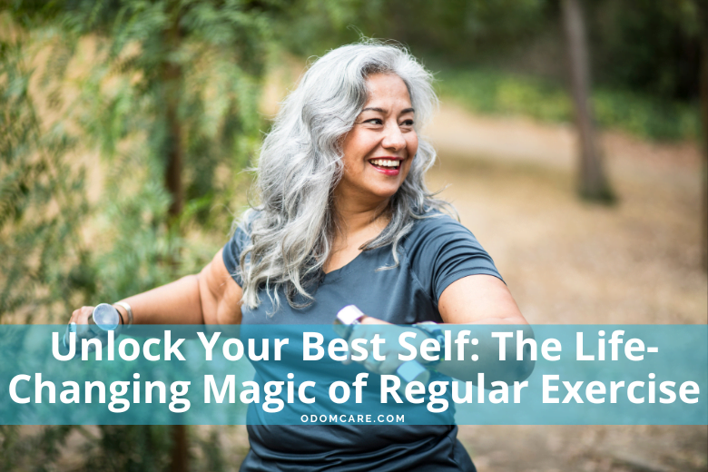 A smiling woman with long, gray hair wearing a blue t-shirt is walking outdoors in a park-like setting, holding dumbbells in her hands.