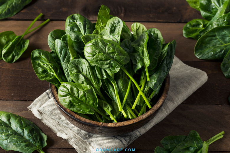 Fresh spinach leaves in a wooden bowl on a wooden table.
